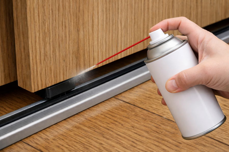 引き戸のレールにシリコンスプレーを吹きかける様子
